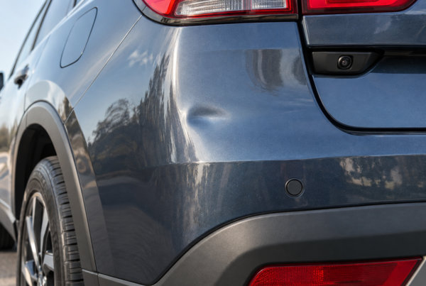 A close-up view of a minor dent on the rear quarter panel of a dark grey SUV, located near a circular parking sensor.